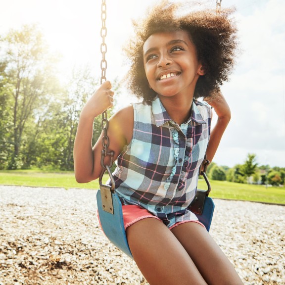 Happy looking child on a swing. The sun is shining behind their head