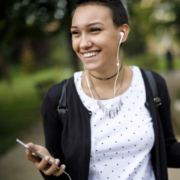 Young person outside smiling. Wearing headphones