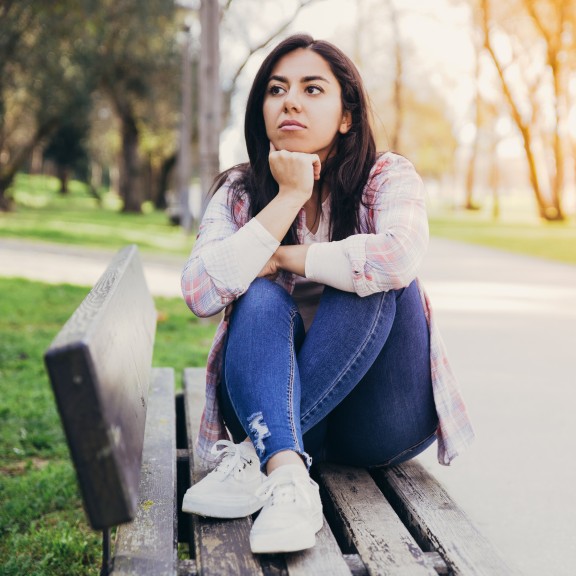 A young person sits thoughtfully outside on a bench