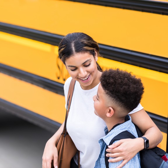 Mother with arm over child's shoulder with school bus in background