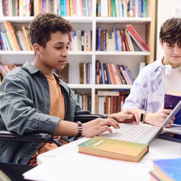 Student in a wheelchair uses laptop in library