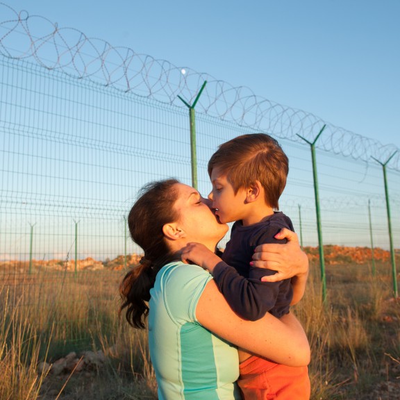 Mother hugging and kissing child near border