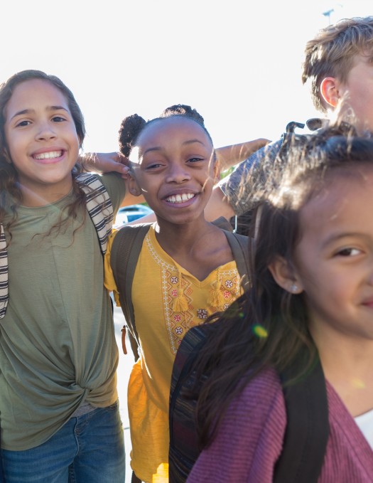 A group of young school children outside with their backpacks on