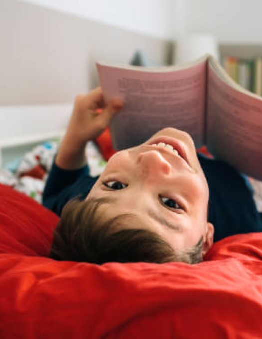 A small child lays on a bed reading a book 