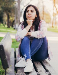 A young person sits thoughtfully outside on a bench