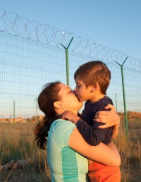 Mother hugging and kissing child near border