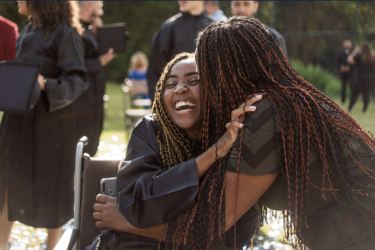 A young person in a wheelchair celebrates graduation with a hug