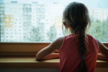 Photo of a child from behind looking out the window