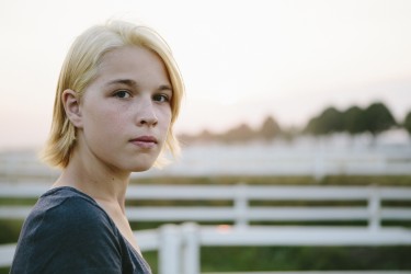 Unsmiling young person with blond hair standing in a pasture